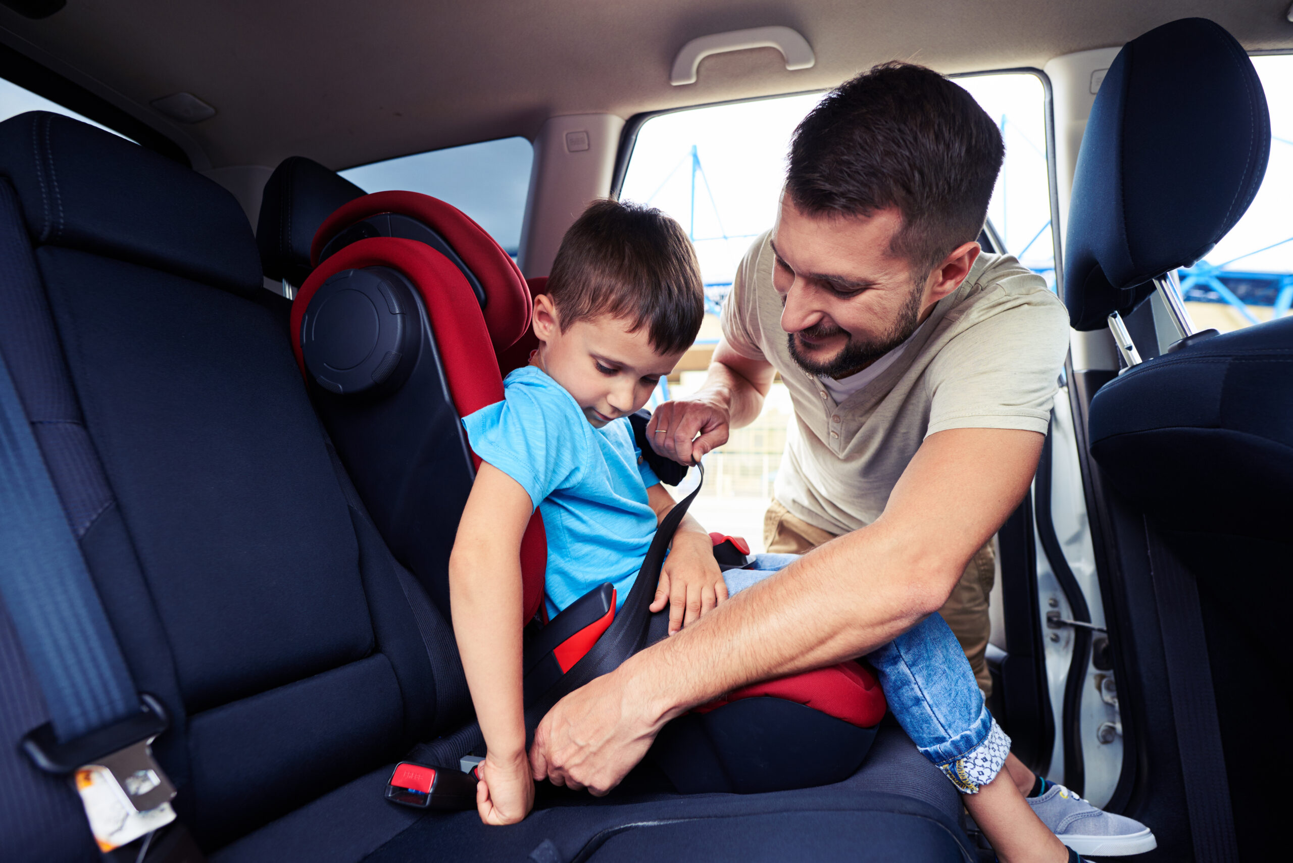 Close-up shot of concentrated father helping his son to fasten belt on car seat