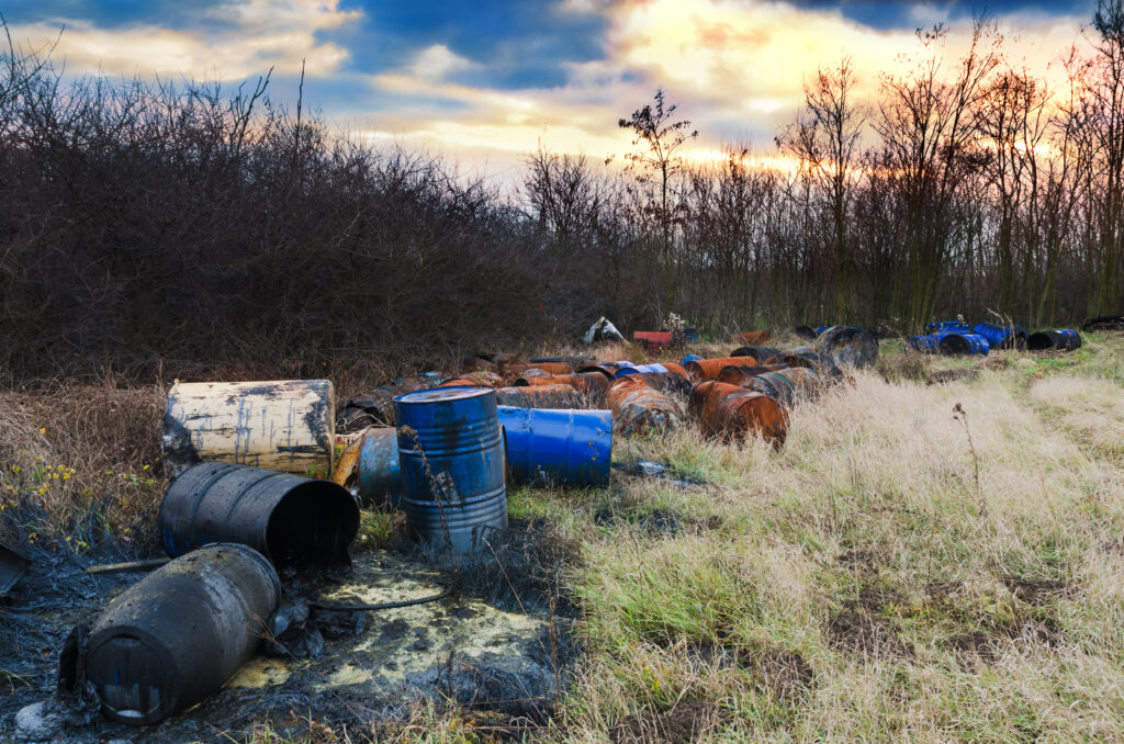Barrels of toxic waste in nature with dramatic sunsets. Environmental pollution.