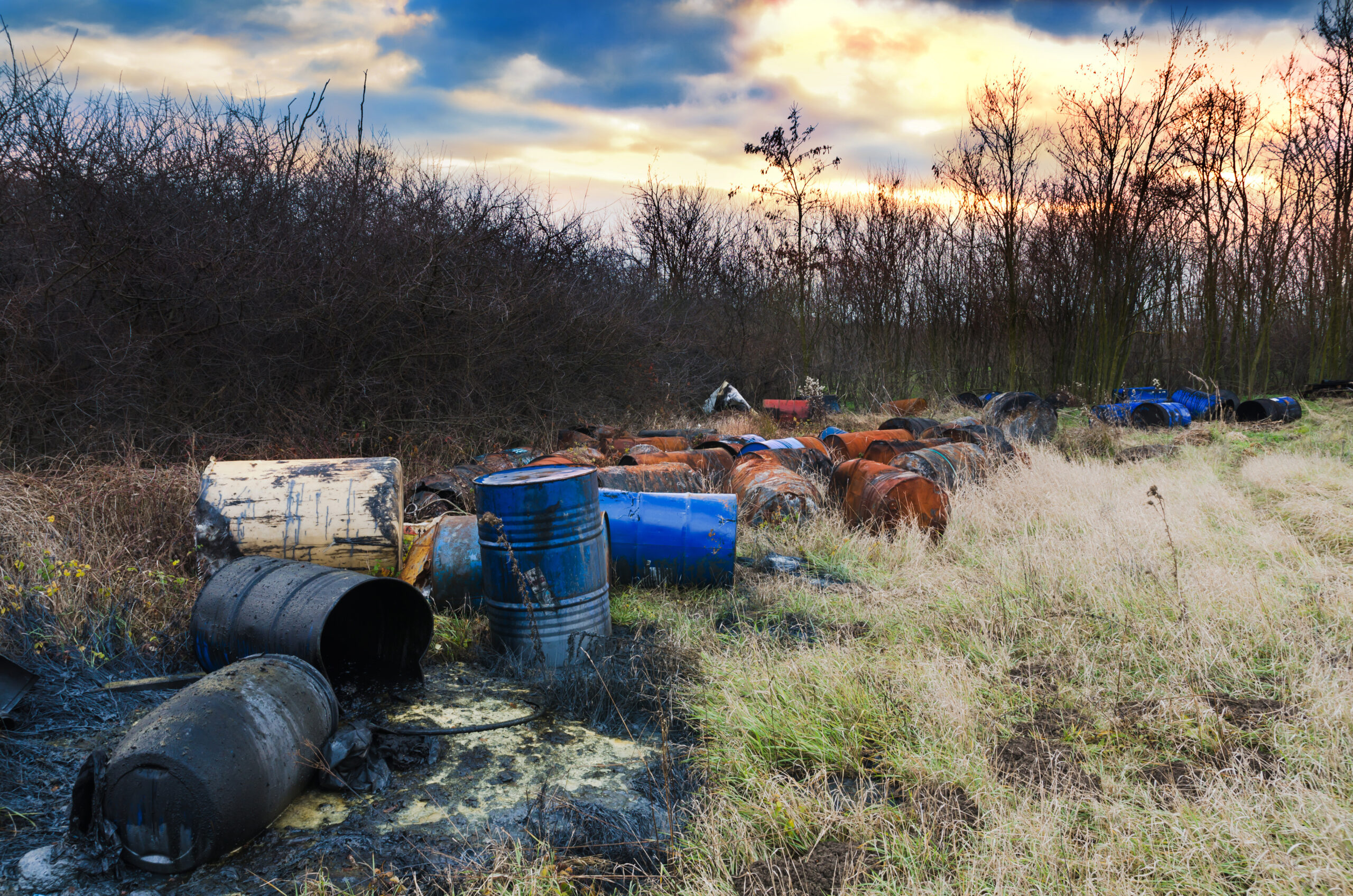 Barrels of toxic waste in nature with dramatic sunsets. Environmental pollution.