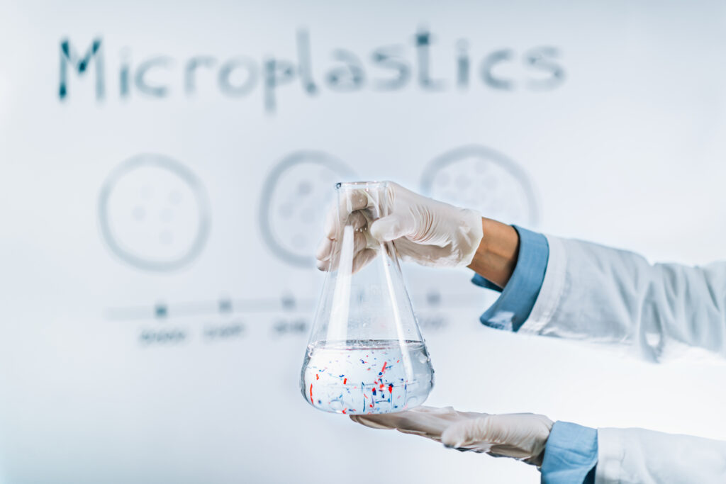 Scientist holding a flask with a water sample full of tiny plastic particles against a whiteboard with microplastic pollution graph.